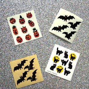 May include: Four square sheets of Halloween-themed stickers. One sheet features orange glittery jack-o'-lanterns with hats. Another shows black bat silhouettes. A third contains black bats on a tan background. The last displays black cats and yellow moons.