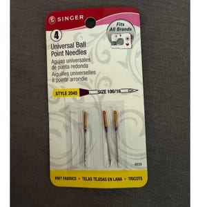 May include: A package of four Singer Universal Ball Point Needles, style 2045, size 100/16. The packaging is white with a red top, featuring text in English, French, and Spanish, and indicates the needles are for knit fabrics.