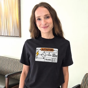 Może przedstawiać: Czarny t-shirt z krótkim rękawem z prostokątną grafiką na klatce piersiowej. Grafika przypomina schemat obwodu elektrycznego z napisem CAUTION, ikoną błyskawicy oraz słowami LOAD: CONTINUOUS SARCASM i nazwą BearTaDa.