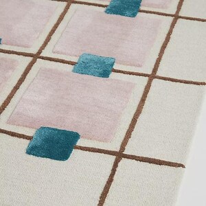 A diagonal corner perspective highlighting the textured pile of the cream, brown, pink, and blue hand-tufted wool rug.