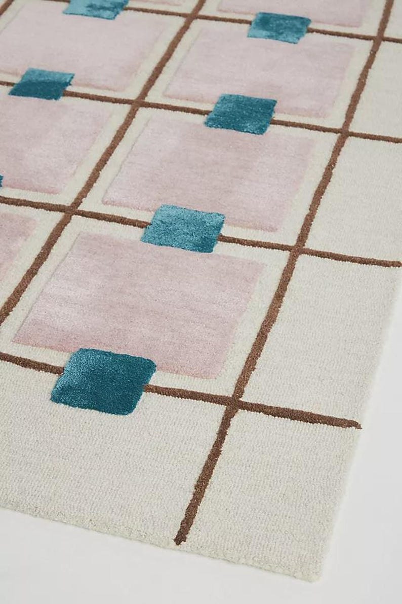 A diagonal corner perspective highlighting the textured pile of the cream, brown, pink, and blue hand-tufted wool rug.