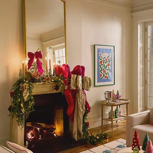 A living room interior featuring the patterned wool rug on the wooden floor in front of a fireplace decorated with holiday garlands and stockings.