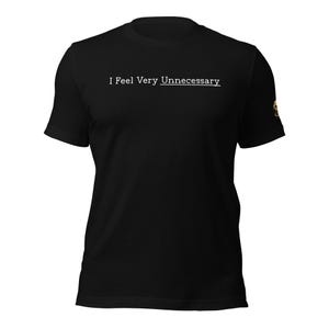May include: A black short-sleeved t-shirt featuring the white text "I Feel Very Unnecessary" printed across the chest, with the word "Unnecessary" underlined. A small, circular gold-colored emblem is visible on the left sleeve of the garment.