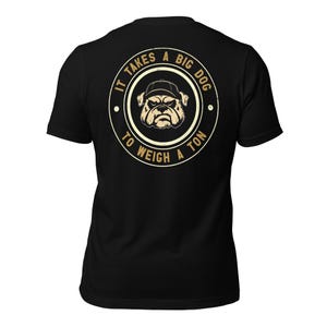 以下が含まれることがあります： 背面に円形のグラフィックが施された黒の半袖Tシャツ。野球帽をかぶったブルドッグのベージュ色のイラストが描かれており、その周囲を「IT TAKES A BIG DOG TO WEIGH A TON」というテキストが円形の枠で囲んでいます。