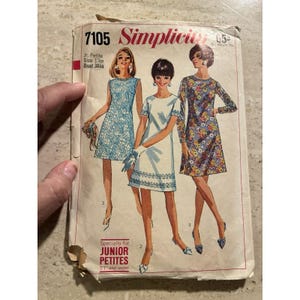 May include: A vintage Simplicity 7105 sewing pattern envelope for a Jr. Petite dress, size 13jp, bust 33. The cover features illustrations of three dresses: a blue floral sleeveless dress, a white short-sleeve dress, and a long-sleeve floral dress.
