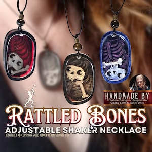 May include: Three handmade necklaces with a skeletal design inside a clear resin pendant. The pendants are attached to black cords with a brown bead. The necklaces are labeled "RATTLED BONES ADJUSTABLE SHAKER NECKLACE".