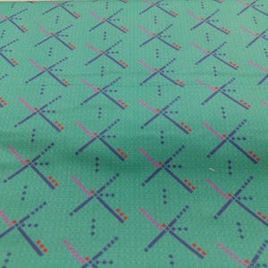 May include: Teal fabric with a repeating geometric pattern. The design features navy blue, pink, and red cross-like shapes, interspersed with small dots. The fabric has a subtle sheen.