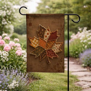 May include: A rectangular garden flag featuring a brown background with a large, central maple leaf applique. The leaf is constructed from various fabric patches in shades of orange, red, yellow, and green, showcasing diverse patterns like gingham and floral.