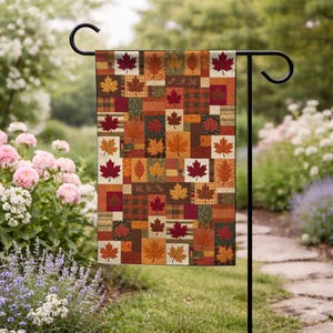 May include: A rectangular garden flag featuring a patchwork design of autumn-themed squares. The pattern displays various maple leaf illustrations in shades of red, orange, yellow, and brown, interspersed with plaid and textured fabric-like blocks.