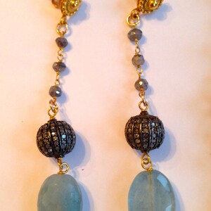 May include: A pair of long, dangling earrings with a light blue gemstone, a black and silver bead, and a gold top.
