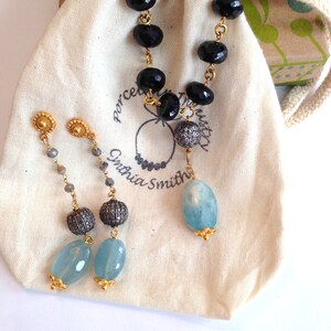 May include: A necklace and earrings set featuring black onyx beads, aquamarine stones, and gold accents. The necklace is in a small white drawstring bag with the text "Porcelain Trust" and "Cynthia Smith" printed on it.
