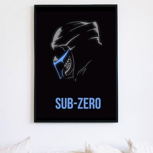 May include: A framed wall art print featuring a black background with a stylized white and blue outline of a masked character head in profile. Below the graphic, the text SUB-ZERO is printed in a bold, light blue sans-serif font.