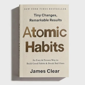 May include: A hardcover book titled Atomic Habits by James Clear with a cream-colored cover and metallic gold lettering. The text reads New York Times Bestseller, Tiny Changes, Remarkable Results, and An Easy & Proven Way to Build Good Habits.