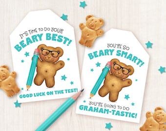 May include: Two printable gift tags featuring a cartoon bear wearing glasses and holding a pencil. The tags are white with blue text and stars. The text on the first tag reads "It's time to do your beary best! Good luck on the test!" The text on the second tag reads "You're so beary smart! You're going to do graham-tastic!"