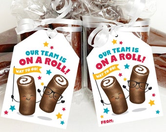 Puede incluir: Etiquetas de regalo imprimibles con dos rollos de canela de dibujos animados con el texto "¡Nuestro equipo está en racha! ¡Buen trabajo!" Las etiquetas son blancas con acentos rojos, azules y amarillos.
