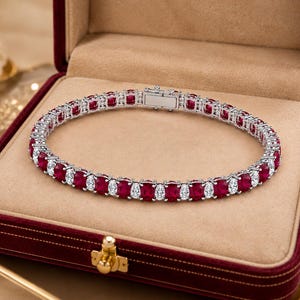 May include: A tennis bracelet featuring alternating oval-cut deep red rubies and smaller round-cut clear white diamonds set in a silver-toned metal band. The bracelet includes a secure box clasp closure and is displayed in a velvet-lined jewellery box.