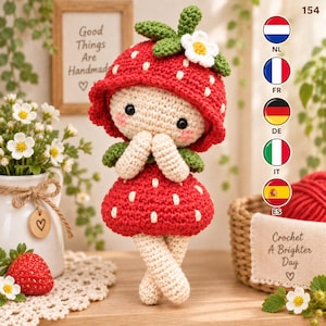 Peut inclure: Une poupée crochetée avec un chapeau rouge en forme de fraise orné d'une fleur blanche et de feuilles vertes, une robe rouge à motifs de fraises et des membres couleur crème. La poupée a des yeux noirs et des joues roses, avec le chiffre 154.