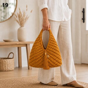 Può includere: Una borsa a mano all'uncinetto color giallo senape con una silhouette triangolare e un motivo a coste testurizzato. La borsa include un ciondolo con nappa giallo senape abbinato attaccato al manico centrale, integrato nel design.