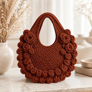 Puede incluir: Un bolso de mano redondo de ganchillo en color óxido, con un cuerpo tejido texturizado y un borde decorativo de múltiples rosetas de ganchillo tridimensionales a lo largo del contorno. El bolso tiene un asa integrada en la parte superior.