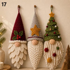 May include: Three hanging crochet gnome ornaments with pointed hats. The left gnome has a maroon hat with holly leaves and berries. The centre gnome has a grey hat with a yellow star. The right gnome has a green tree-shaped hat with small ornaments.