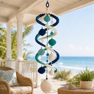 May include: A hanging spiral mobile featuring crocheted yarn in shades of navy blue, teal, and cream. The structure is adorned with various crocheted seashell shapes and small wooden beads, suspended by a central cord with a large shell at the base.
