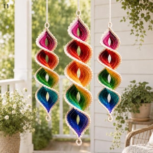 Pode incluir: Três ornamentos em espiral suspensos com um vibrante gradiente de cores do arco-íris, incluindo magenta, vermelho, laranja, amarelo, verde e azul. Cada peça é construída com uma textura de crochê e finalizada com uma borda cor de creme.
