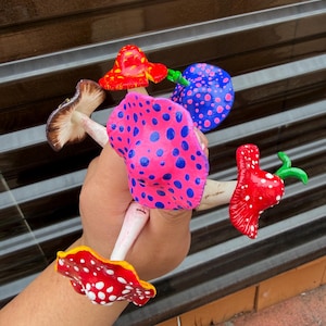 May include: A collection of six small, hand-painted mushroom figurines featuring various colors including bright pink with blue spots, red with white spots, blue with pink spots, and a brown-capped mushroom with visible white gills on the underside.