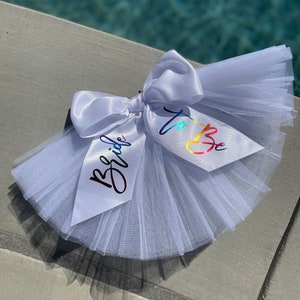 May include: White tulle bridal sash with a white satin bow and rainbow lettering that says "Bride to Be".