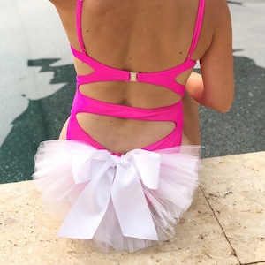 May include: A pink swimsuit with a cut-out design and a white tulle skirt with a large white bow.