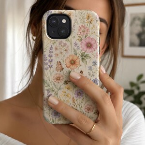 May include: A smartphone case featuring a cream-colored background with a delicate botanical print of various wildflowers in shades of pink, purple, and orange, accented by a small butterfly and a bee, with a black camera lens cutout at the top.