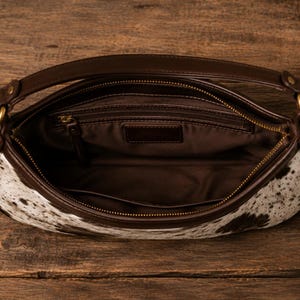 Interior view of cowhide hobo satchel shoulder bag showing brown fabric lining, zip pocket, and leather trim