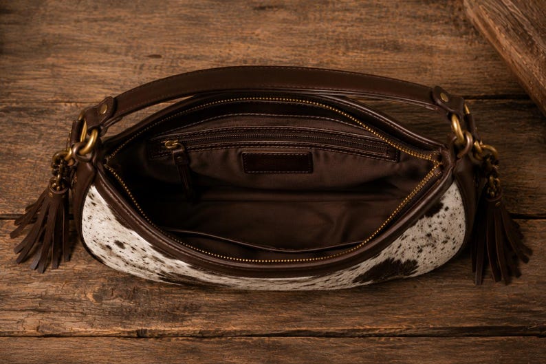 Interior view of cowhide hobo satchel shoulder bag showing brown fabric lining, zip pocket, and leather trim