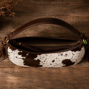 Open cowhide leather hobo bag with brass zipper, tassel pulls, and striped brown interior lining