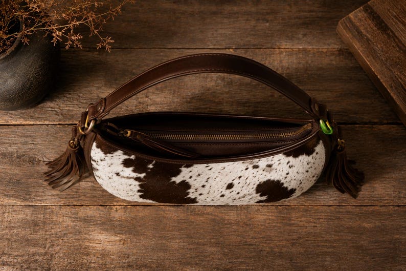 Open cowhide leather hobo bag with brass zipper, tassel pulls, and striped brown interior lining