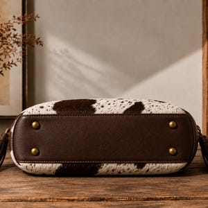 Bottom view of cowhide hobo bag showing reinforced leather base, brass studs, and hanging leather tassels