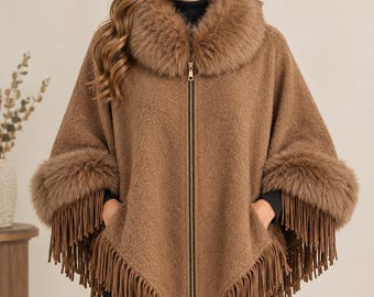May include: A tan, textured poncho featuring a full-length front zipper, a thick faux fur collar, and matching faux fur cuffs. The hemline is adorned with long, dangling fringe trim that extends around the entire bottom edge of the garment.