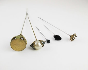 May include: Five vintage hat pins with decorative tops. The tops include a pearl, a black velvet square, a gold floral design, a gold crown, and a black bead.