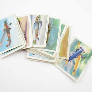 May include: A collection of vintage trading cards featuring illustrations of different airplanes. The cards are in various colors, including green, blue, yellow, and red. The cards have text on them, including the names of the airplanes and their manufacturers.