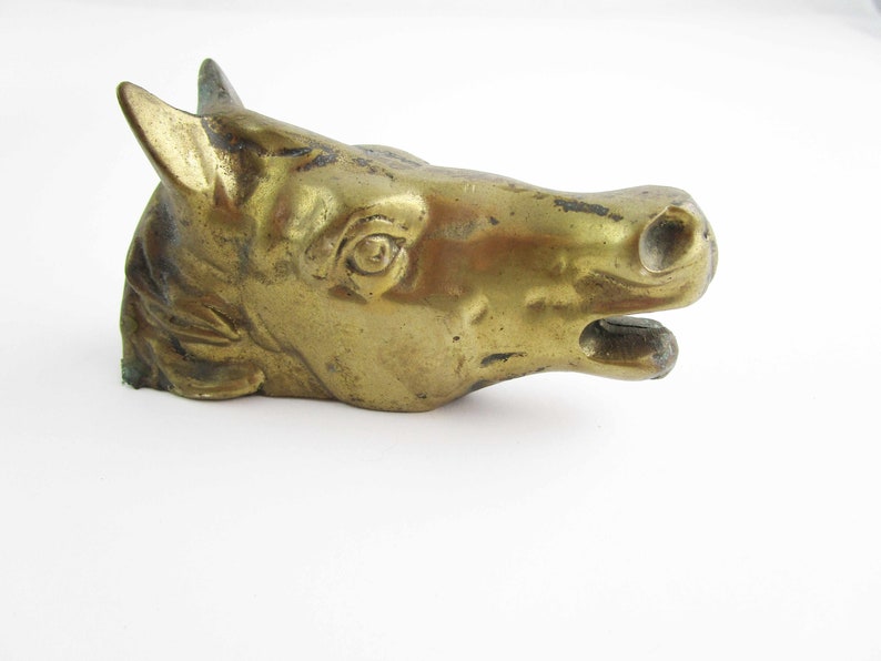 May include: A gold-colored metal horse head sculpture. The horse's mouth is open and its eyes are detailed.