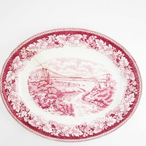 May include: A white oval platter with a red floral border and a red and white image of a bridge and river.