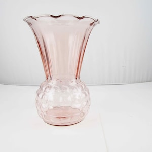 May include: A pink glass vase with a ruffled rim and a textured, bubble-like pattern on the lower portion. The vase has a flared shape and stands on a white surface.
