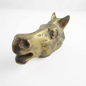 May include: A brass horse head sculpture with a distressed finish. The horse's head is tilted to the side, and its mouth is slightly open.