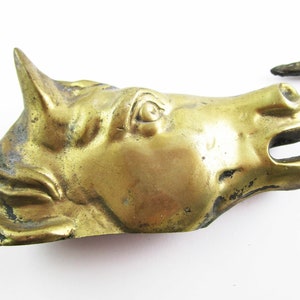 May include: A gold-colored metal horse head sculpture. The horse's eye is detailed and the sculpture has a worn, antique look.