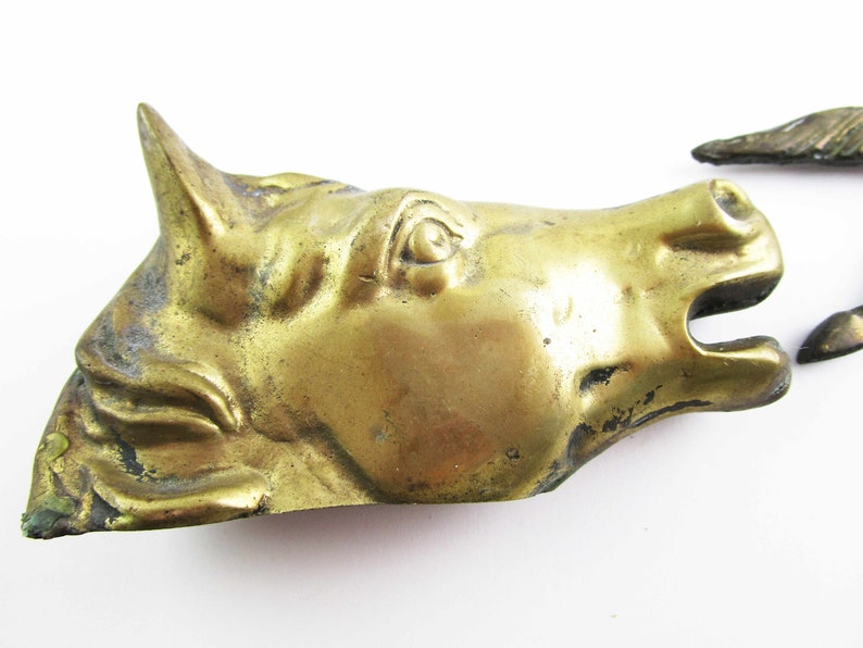 May include: A gold-colored metal horse head sculpture. The horse's eye is detailed and the sculpture has a worn, antique look.
