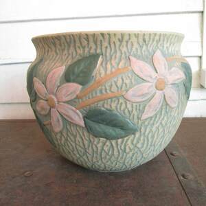 May include: A ceramic planter with a green and brown textured surface and pink flowers in relief.