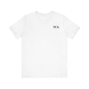 May include: A plain white short-sleeve t-shirt featuring the letters TCG printed in a simple black serif font on the upper left chest area. The garment has a standard crew neckline and a clean, solid white fabric construction throughout.