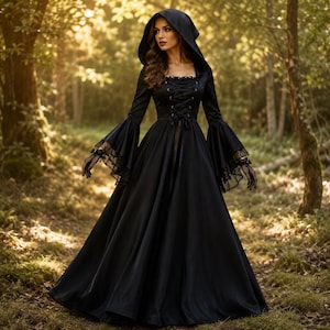 May include: A floor-length black dress featuring a hood, long flared sleeves with lace trim, and a lace-up corset-style bodice. The garment has a square neckline and a full, flowing skirt that reaches the ground, creating a structured silhouette.
