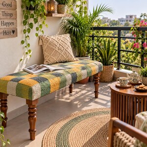 Puede incluir: Un banco rectangular con patas de madera torneada y un asiento texturizado de cuadros multicolores en tonos amarillo, verde y crema. Un libro abierto descansa sobre el asiento, acompañado de un cojín color crema con patrón de rombos.