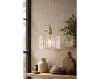 May include: A pendant light fixture featuring a clear, vertically ribbed glass shade suspended by a twisted fabric cord from a brass-toned metal socket. The light emits a warm glow from the center, highlighting the textured glass surface.