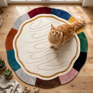 May include: A round area rug featuring a cream-coloured centre with embossed swirling lines and a multi-coloured border composed of segments in red, blue, yellow, green, black, pink, brown, grey, and teal. A fluffy orange cat stands on the rug.